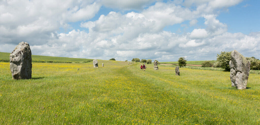 A scenic view of a grassy field with large standing stones in a row, under a partly cloudy sky.