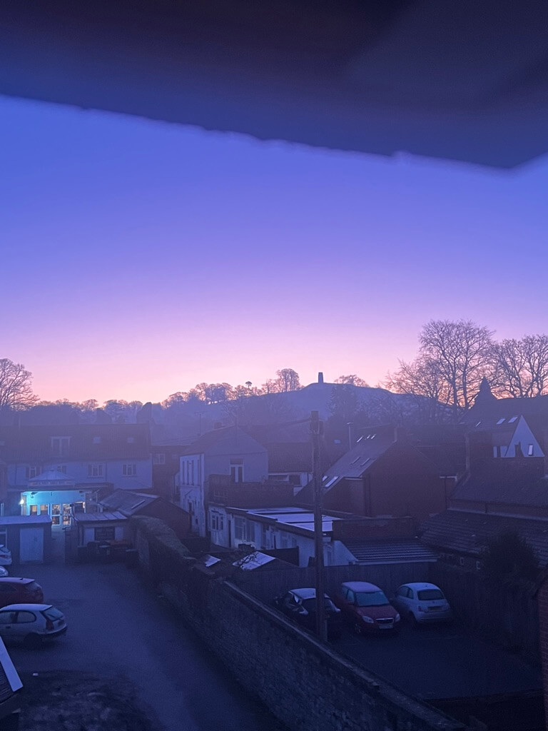 Early morning sky transitioning from purple to orange over a quiet neighborhood.