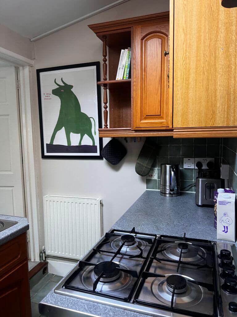 Kitchen corner with a four-burner gas stove, wooden cabinets, kettle, and a wall-mounted image of a green bull.